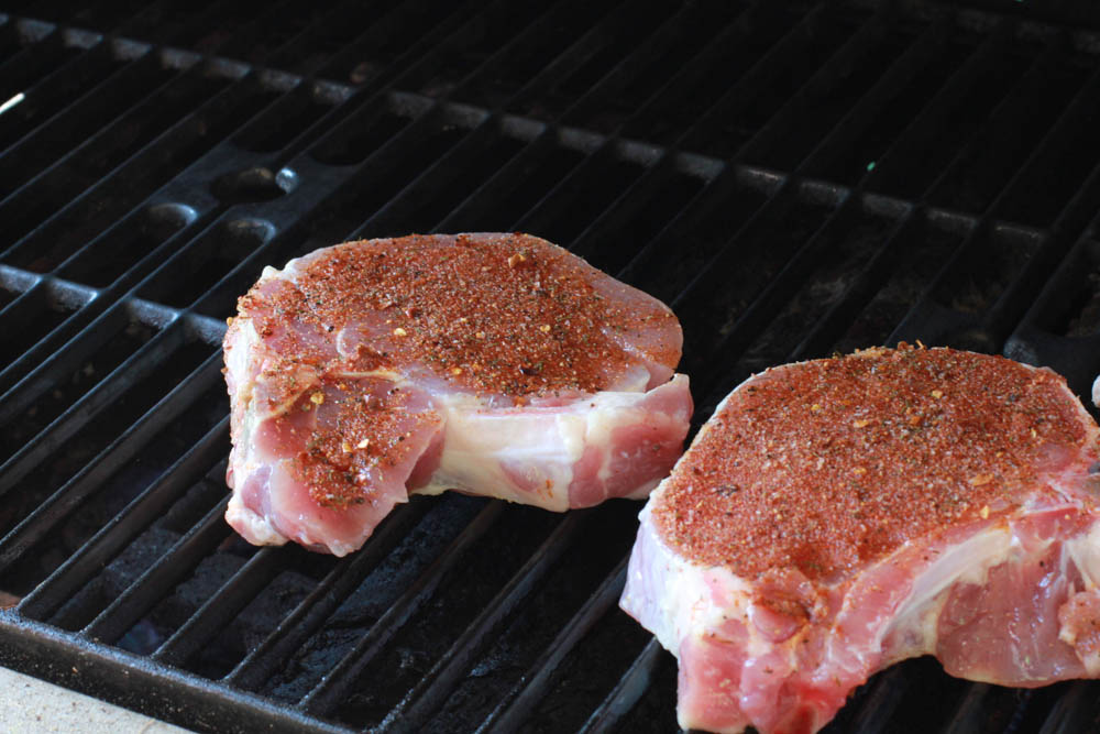 2 porterhouse pork chops on the grill with a homemade steak rub on them