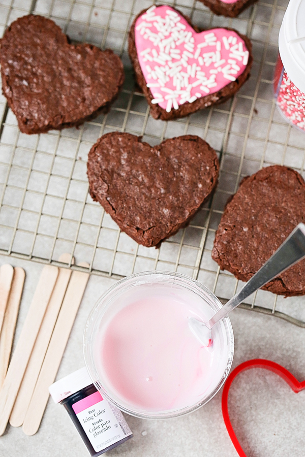 a tray of heart shaped cookies with a bowl of pink icing