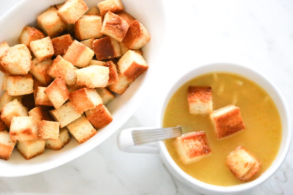 A white bowl of chicken noodle soup with a few easy homemade croutons over the top.