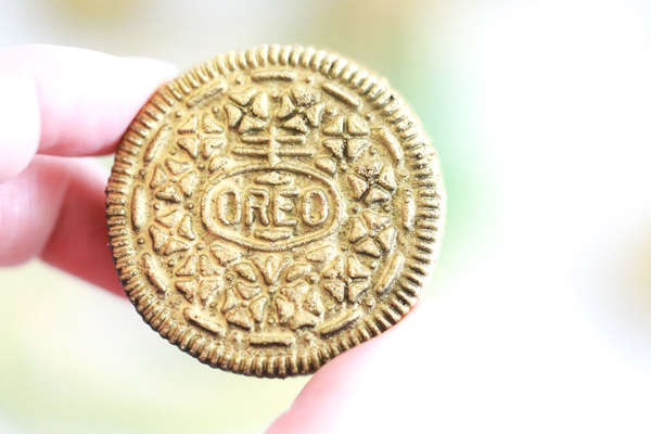 person holding gold covered oreo in their hand