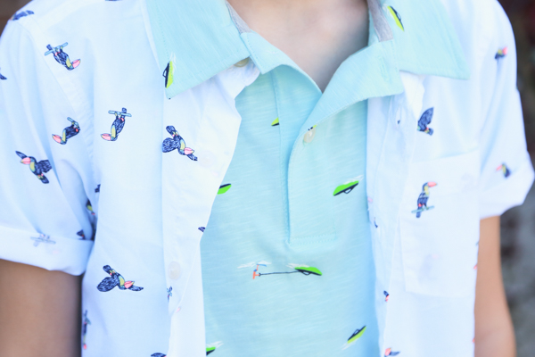 a child wearing a blueish green polo shirt with boats on it and a white button up shirt with toucans layered over it - perfect spring styles at oshkosh b'gosh