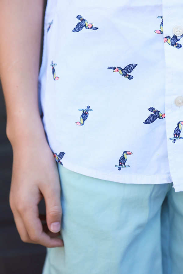 a child wearing blueish shorts with a white button up shirt with toucans on it - perfect spring styles at oshkosh b'gosh